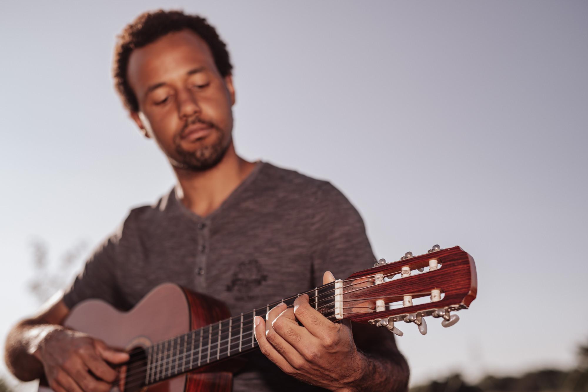 Eddie Talanga spielt Gitarre vor klarem blauem Himmel